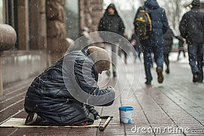 Hungry homeless beggar woman beg for money on the urban street in the city from people walking by Stock Photo