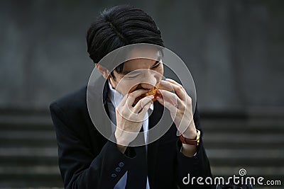 Hungry male office worker in formal wear sitting on stairs outside office and eating tasty sandwiches during lunch Stock Photo