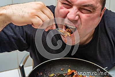 A hungry man eagerly eats fried meat with sauce from a fork Stock Photo