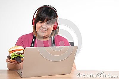 Hungry overweight woman smiling and holding a hamburger in the living room While work from home, her very happy and enjoy to eat Stock Photo