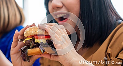 Hungry overweight woman smiling and holding hamburger and sitting in the living room, her very happy and enjoy to eat fast food. C Stock Photo