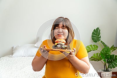 Hungry overweight young asian woman holding hamburger, Her hungry all time and overeat, gluttony and binge eating. Her lifestyle Stock Photo