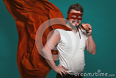 Hungry super hero man eating a hamburger, super hero or antihero in a red suit with a flying cloak eats fast food Stock Photo