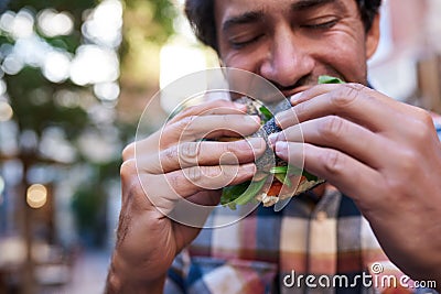 Hungry young man sitting outside biting into a delicious bagel Stock Photo