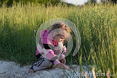 Hunkering little girl playing in field dirt outdoors at natural green meadow grass backdrop Stock Photo