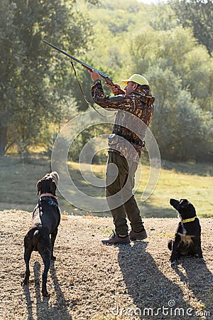 A hunter with a gun in his hands in hunting clothes in the autumn forest in search of a trophy. Stock Photo