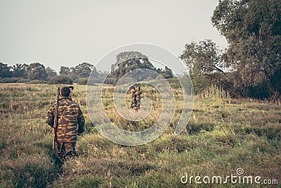 Hunters crossing through tall grass in rural field during hunting season Stock Photo