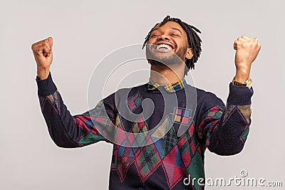 Hurray! Extremely satisfied happy african man with dreadlocks rising hands up with toothy smile on face, pleased, amazed with Stock Photo