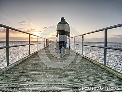 Hurt man with hooded jacket and forearm crutches looking sadly Stock Photo