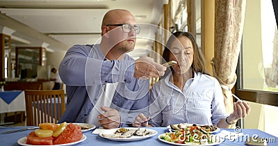 The husband bald and in glasses and the dark-haired middle-aged wife, sit in cafe, eat, laugh, communicate. A man pulls Stock Photo