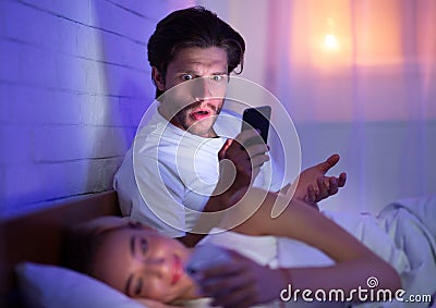 Husband Catching Wife Chatting On Phone In Bed At Night Stock Photo