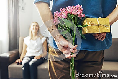Husband hiding romantic surprise present and flowers behind back to beloved wife Stock Photo