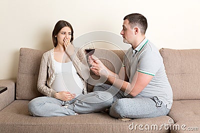 Husband offers a glass of red wine to his pregnant wife but she refuses and makes stop gesture because she feels sick. Feeling bad Stock Photo