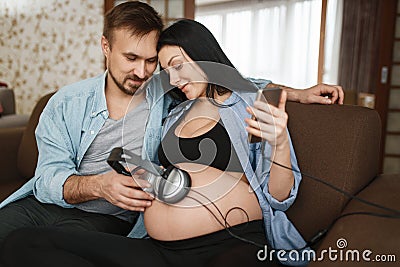 Husband and pregnant wife with headphones at belly Stock Photo