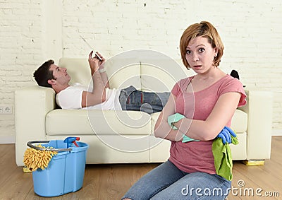 Husband resting on couch while wife cleaning doing housework in chauvinism concept Stock Photo