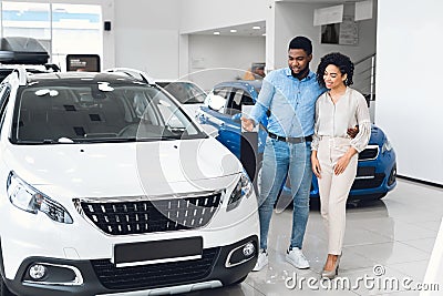 Husband Showing Wife New Auto Standing In Showroom, Full Length Stock Photo