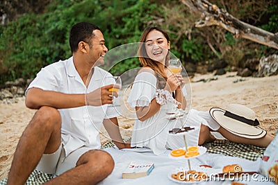 husband and wife chatting holding drink glasses sitting on a blanket picnicking Stock Photo