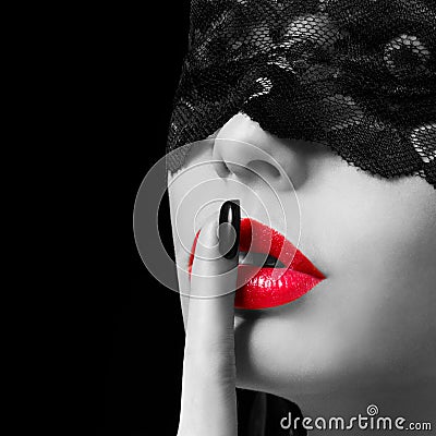 Hush. woman with finger on her red lips showing shush. Erotic girl with lace mask over black background. Stock Photo