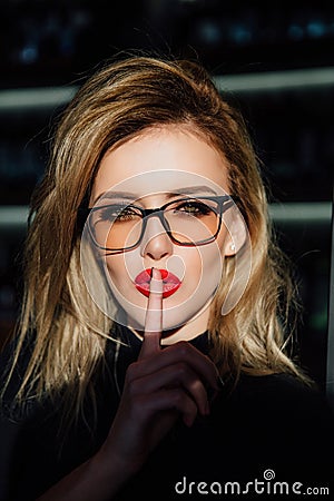 Hush. Woman in glasses ask for silence or secrecy with finger on red lips. shh hand gesture. Stock Photo