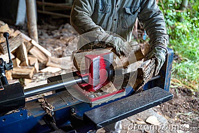 Hydraulic log splitter blade cuts into wood with workman and woodpile Stock Photo