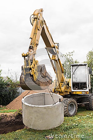 Hydraulic piston system excavator with a bucket, lifting on steel cable concrete sewer ring. Repairs or sewage works on an Stock Photo