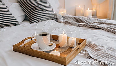Hygge concept Coffee and candle filled wooden tray on a bed accompanied by white bedding striped blanket and pillow serving Stock Photo