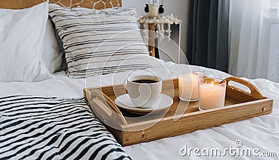 Hygge concept Coffee and candle filled wooden tray on a bed accompanied by white bedding striped blanket and pillow serving Stock Photo