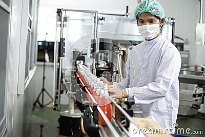 Hygiene worker working in drink factory at conveyor belt with fruit juice glass bottled in production line Stock Photo