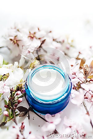 Hygienic skincare lotion product. Herbal spa cosmetic cream with pink cherry flowers in a blue glass jar Stock Photo