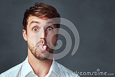 I can be a bit of a goofball. Studio portrait of a handsome young man sticking his tongue out against a dark background. Stock Photo