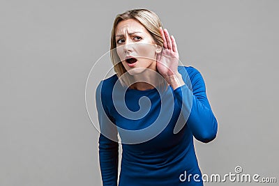 I can`t hear! Portrait of curious attentive woman keeping hand near ear. indoor studio shot isolated on gray background Stock Photo