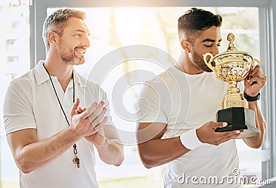 I cant think of anyone more deserving. a handsome young male tennis player kissing a trophy while his coach watches on Stock Photo