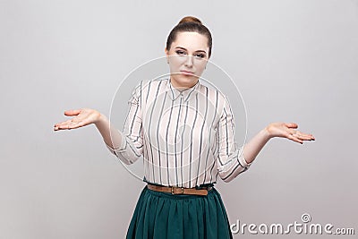 I don`t know. Confused beautiful young woman in striped shirt and green skirt with makeup and collected ban hairstyle, standing Stock Photo