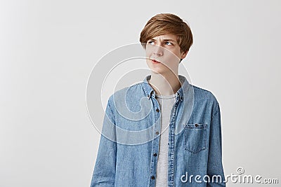 I don`t know. Doubtful caucasian young male wearing denim shirt, pouting lips and looking up with indecisive expression Stock Photo