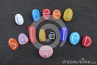 I feel satiated, creative text composed with multi colored and carved sea stones over black volcanic sand Stock Photo