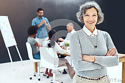 I leave the presentations to him. Portrait of a businesswoman standing with her arms folded in the boardroom while a Stock Photo