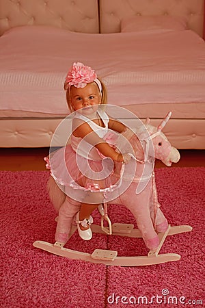 I love this horse. Small blond girl ride toy horse. Small child wear hair band. Little girl with long hairstyle. Hair Stock Photo