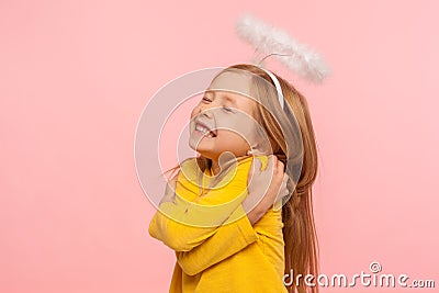 I love myself. Beautiful charming little girl with halo over head embracing herself and smiling from happiness Stock Photo