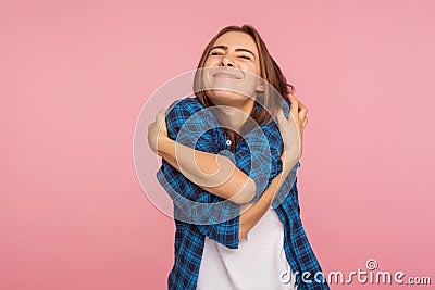 I love myself! Portrait of charming girl in checkered shirt hugging herself tightly and smiling with pleasure Stock Photo