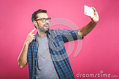 I love selfie! Handsome young man in shirt holding camera and making selfie and smiling while standing against pink background. Stock Photo