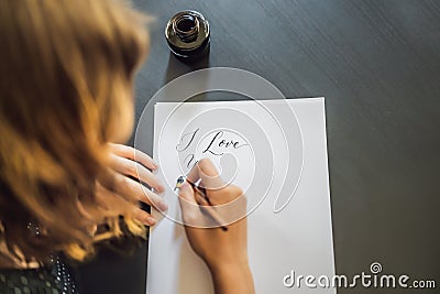 I love you. Calligrapher Young Woman writes phrase on white paper. Inscribing ornamental decorated letters. Calligraphy Stock Photo