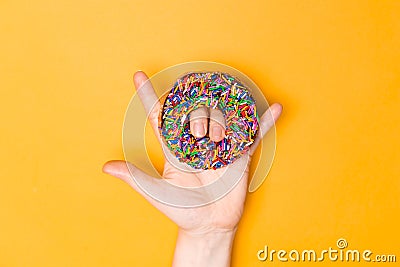 I love you hand sign with chocolate frosted donut with sprinkles, sugar-glazed frosted on yellow background. Playful and joyful Stock Photo