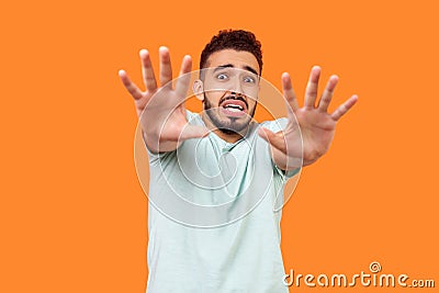 I`m afraid! Portrait of scared terrified brunette man making frightened gesture with raised hands. isolated on orange background Stock Photo