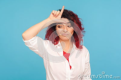 I`m loser! Portrait of unlucky depressed hipster woman with fancy red hair showing L sign on forehead Stock Photo