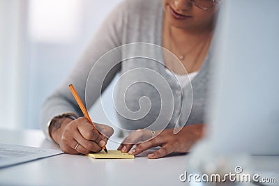 I make notes so I dont forget anything. an unrecognizable businesswoman sitting alone in her office and writing on a Stock Photo