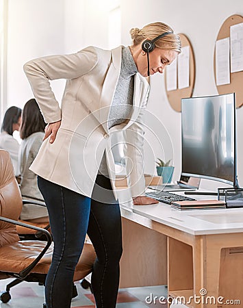 I think I need to stand up. an attractive mature female call center agent suffering with back pain while working on her Stock Photo