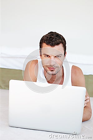 I think I should work from home today...A handsome man lying on his bed working on his laptop. Stock Photo