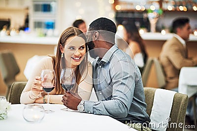 I think we should book a hotel room. an affectionate young man whispering into his girlfriends ear while sitting in a Stock Photo