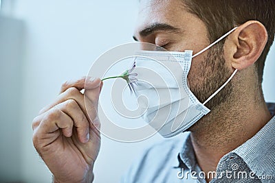 I wish I could smell this flower. a unrecognizable young man wearing a surgical mask while trying to smell a flower Stock Photo