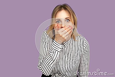 I won`t say anyone! Frightened blond woman covering her mouth with arm and looking at camera with scared big eyes Stock Photo